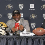 
              Deion Sanders, center, uses his mobile telephone to illustrate how Rick George, right, Colorado athletic director, kept in touch while courting Sanders to become the new head football coach at Colorado during a news conference Sunday, Dec. 4, 2022, in Boulder, Colo. Colorado chancellor Phil DeStefano, left, looks on. Sanders left Jackson State University after three seasons at the helm of the school's football team. (AP Photo/David Zalubowski)
            