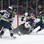 Arizona Coyotes goalie Karel Vejmelka (70) stops Vancouver Canucks' Elias Pettersson (40) as Canucks' Ilya Mikheyev (65) falls and Canucks' Janis Moser (90) defends during the third period of an NHL hockey game Saturday, Dec. 3, 2022, in Vancouver, British Columbia. (Darryl Dyck/The Canadian Press via AP)