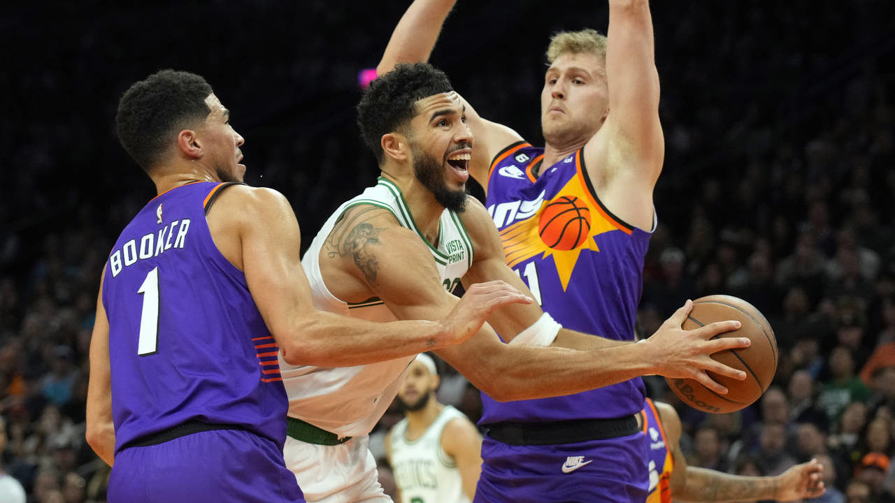 Boston Celtics forward Jayson Tatum (0) drives between Phoenix Suns guard Devin Booker (1) and cent...