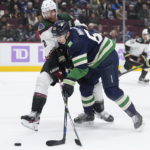 Arizona Coyotes' Patrik Nemeth (2), of Sweden, and Vancouver Canucks' Ilya Mikheyev (65), of Russia, vie for the puck during the first period of an NHL hockey game in Vancouver, British Columbia on Saturday, Dec. 3, 2022. (Darryl Dyck/The Canadian Press via AP)