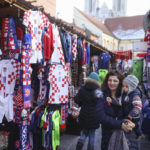 
              A woman carrying her child walks among shops selling Croatian football jerseys and various fan props, prior to the Qatar World Cup semi-final match between Croatia and Argentina, in Zagreb, Croatia, Tuesday, Dec. 13, 2022. (AP Photo/Armin Durgut)
            