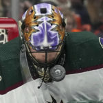 Arizona Coyotes goalie Karel Vejmelka, of the Czech Republic, is struck in the mask by the puck during the first period of an NHL hockey game against the Vancouver Canucks in Vancouver, British Columbia on Saturday, Dec. 3, 2022. (Darryl Dyck/The Canadian Press via AP)