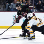 Arizona Coyotes defenseman Josh Brown, left, sends the puck past Boston Bruins left wing Jake DeBrusk, right, for a goal during the first period of an NHL hockey game in Tempe, Ariz., Friday, Dec. 9, 2022. (AP Photo/Ross D. Franklin)