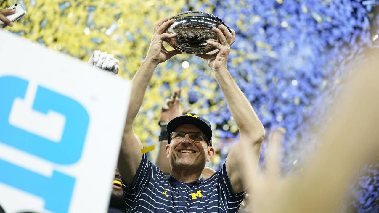 Michigan head coach Jim Harbaugh holds the trophy after defeating Purdue in the Big Ten championshi...