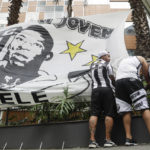 
              Santos soccer team supporters secure a banner with the image of former soccer star Pele, in front of the Albert Einstein hospital where he is hospitalized in Sao Paulo, Brazil, Sunday, Nov. 4, 2022. The 82-year-old Pele has been at the hospital since Tuesday and officials say he is responding well to treatment for a respiratory infection. (AP Photo/Marcelo Chello)
            