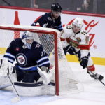 
              Florida Panthers' Matthew Tkachuk (19) carries the puck behind Winnipeg Jets goaltender Connor Hellebuyck (37) during the first period of an NHL hockey game Tuesday, Dec. 6, 2022, in Winnipeg, Manitoba. (Fred Greenslade/The Canadian Press via AP)
            