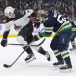 Arizona Coyotes' Patrik Nemeth (2), of Sweden, and Vancouver Canucks' Ilya Mikheyev (65), of Russia, skate after the puck during the first period of an NHL hockey game in Vancouver, British Columbia on Saturday, Dec. 3, 2022. (Darryl Dyck/The Canadian Press via AP)