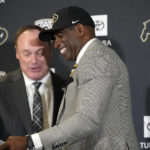 Deion Sanders, front, is welcomed to the podium by Colorado atheltic director Rick George after introducing Sanders as the new head football coach at the University of Colorado during a news conference Sunday, Dec. 4, 2022, in Boulder, Colo. Sanders left Jackson State University after three seasons at the helm of the school's football team. (AP Photo/David Zalubowski)