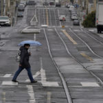 
              FILE - A pedestrian carries an umbrella while crossing a street in San Francisco, Thursday, April 14, 2022.  A variety of new laws take effect Sunday, Jan. 1, 2023 that could have an impact on people's finances and, in some cases, their personal liberties. (AP Photo/Jeff Chiu, File)
            