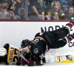 Arizona Coyotes right wing Christian Fischer (36) falls over Boston Bruins defenseman Hampus Lindholm (27) during the first period of an NHL hockey game in Tempe, Ariz., Friday, Dec. 9, 2022. The Coyotes won 4-3. (AP Photo/Ross D. Franklin)