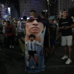 An Argentina soccer fan wears a banner with the image the late soccer star Diego Armando Maradona, during the celebration after the team defeated Croatia in the semifinal World Cup match, in downtown Buenos Aires, Argentina, Tuesday, Dec. 13, 2022. (AP Photo/Rodrigo Abd)