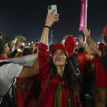 Morocco soccer team fan uses her mobile phone as supporters cheer while they their walk towards Al Bayt Stadium prior of the World Cup semifinals soccer match between France and Morocco in Doha, Qatar, Wednesday, Dec. 14, 2022. (AP Photo/Frank Augstein)