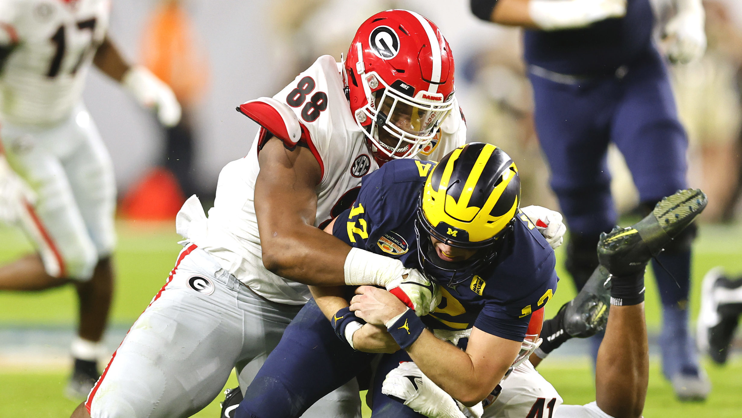 Cade McNamara #12 of the Michigan Wolverines is tackled by Channing Tindall #41 and Jalen Carter #8...