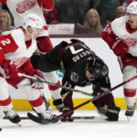Arizona Coyotes center Nick Bjugstad (17) gets upended by Detroit Red Wings defenseman Olli Maatta (2) as Wings defenseman Gustav Lindstrom (28) skates to the puck during the first period of an NHL hockey game in Tempe, Ariz., Tuesday, Jan. 17, 2023. (AP Photo/Ross D. Franklin)