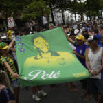 
              People hold a banner of the late Brazilian soccer great Pele along the route of his funeral procession from Vila Belmiro stadium to the cemetery in Santos, Brazil, Tuesday, Jan. 3, 2023. (AP Photo/Matias Delacroix)
            