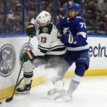 Minnesota Wild center Sam Steel (13) and Tampa Bay Lightning center Anthony Cirelli (71) battle for the puck along the dasher during the first period of an NHL hockey game Tuesday, Jan. 24, 2023, in Tampa, Fla. (AP Photo/Chris O'Meara)