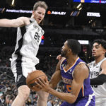 Phoenix Suns' Mikal Bridges, center, looks to pass the ballas he is defended by San Antonio Spurs' Jakob Poeltl (25) and Tre Jones during the second half of an NBA basketball game, Saturday, Jan. 28, 2023, in San Antonio. (AP Photo/Darren Abate)