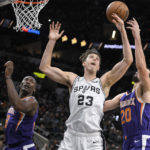 San Antonio Spurs' Zach Collins (23) and Phoenix Suns' Dario Saric (20) fight for possession as Suns' Bismack Biyombo watches during the first half of an NBA basketball game, Saturday, Jan. 28, 2023, in San Antonio. (AP Photo/Darren Abate)