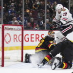 Chicago Blackhawks' Jason Dickinson (17) jumps over Vancouver Canucks goalie Collin Delia (60) and Tyler Myers to avoid a collision during the second period of an NHL hockey game Tuesday, Jan. 24, 2023, in Vancouver, British Columbia. (Darryl Dyck/The Canadian Press via AP)