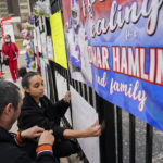 Kayla Adeniji, center, wife of Cincinnati Bengals offensive lineman Hakeem Adeniji, tapes up a sign she made in support of Buffalo Bills safety Damar Hamlin outside UC Medical Center, Thursday, Jan. 5, 2023, in Cincinnati. Hamlin, who remains hospitalized at the center, has shown what physicians treating him are calling "remarkable improvement over the last 24 hours," the team announced on Thursday, three days after the player went into cardiac arrest and had to be resuscitated on the field. (AP Photo/Joshua A. Bickel)