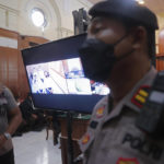 
              Police officers stand near a monitor inside a court room during a trial in Surabaya, East Java, Indonesia , Monday, Jan, 16, 2023. The court began a trial Monday against five men on charges of negligence leading to deaths of 135 people after police fired tear gas inside a soccer stadium, setting off a panicked run for the exits in which many were crushed. (AP Photo/Trisnadi)
            