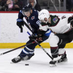 Arizona Coyotes defenseman Shayne Gostisbehere (14) and Winnipeg Jets center Cole Perfetti (91) battle for the puck during second-period NHL hockey game action in Winnipeg, Manitoba, Sunday, Jan. 15, 2023. (Fred Greenslade/The Canadian Press via AP)