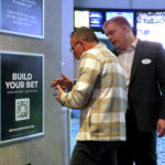 
              An employee at the Ocean Casino Resort, right, in Atlantic City, N.J., helps a customer use a cell phone to scan a sports betting code Monday, Feb. 6, 2023. On Feb. 7, 2023, the gambling industry's national trade group, the American Gaming Association, predicted that over 50 million American adults will bet a total of $16 billion on this year's Super Bowl, including legal bets with sports books, illegal ones with bookies, and casual bets among friends or relatives. (AP Photo/Wayne Parry)
            