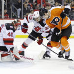 
              New Jersey Devils goaltender Akira Schmid, left, defends as Devils' Ryan Graves (33) battles for the puck with Philadelphia Flyers defenseman Rasmus Ristolainen, right, during the first period of an NHL hockey game Saturday, Feb. 25, 2023, in Newark, N.J. (AP Photo/Adam Hunger)
            