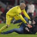 
              Sevilla's goalkeeper Marko Dmitrovic, top, pushes back a PSV supporter after being punched in the face during the Europa League playoff second leg soccer match between PSV and Sevilla at the Philips stadium in Eindhoven, Netherlands, Thursday, Feb. 23, 2023. Sevilla won 3-2 on aggregate. (AP Photo/Peter Dejong)
            