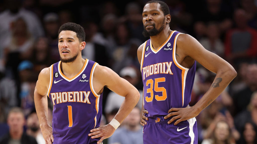 Devin Booker #1 and Kevin Durant #35 of the Phoenix Suns stand on the court during a timeout form t...