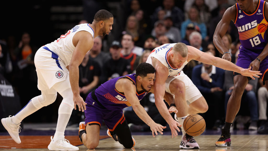 Devin Booker #1 of the Phoenix Suns and Mason Plumlee #44 of the LA Clippers dive for a loose ball ...