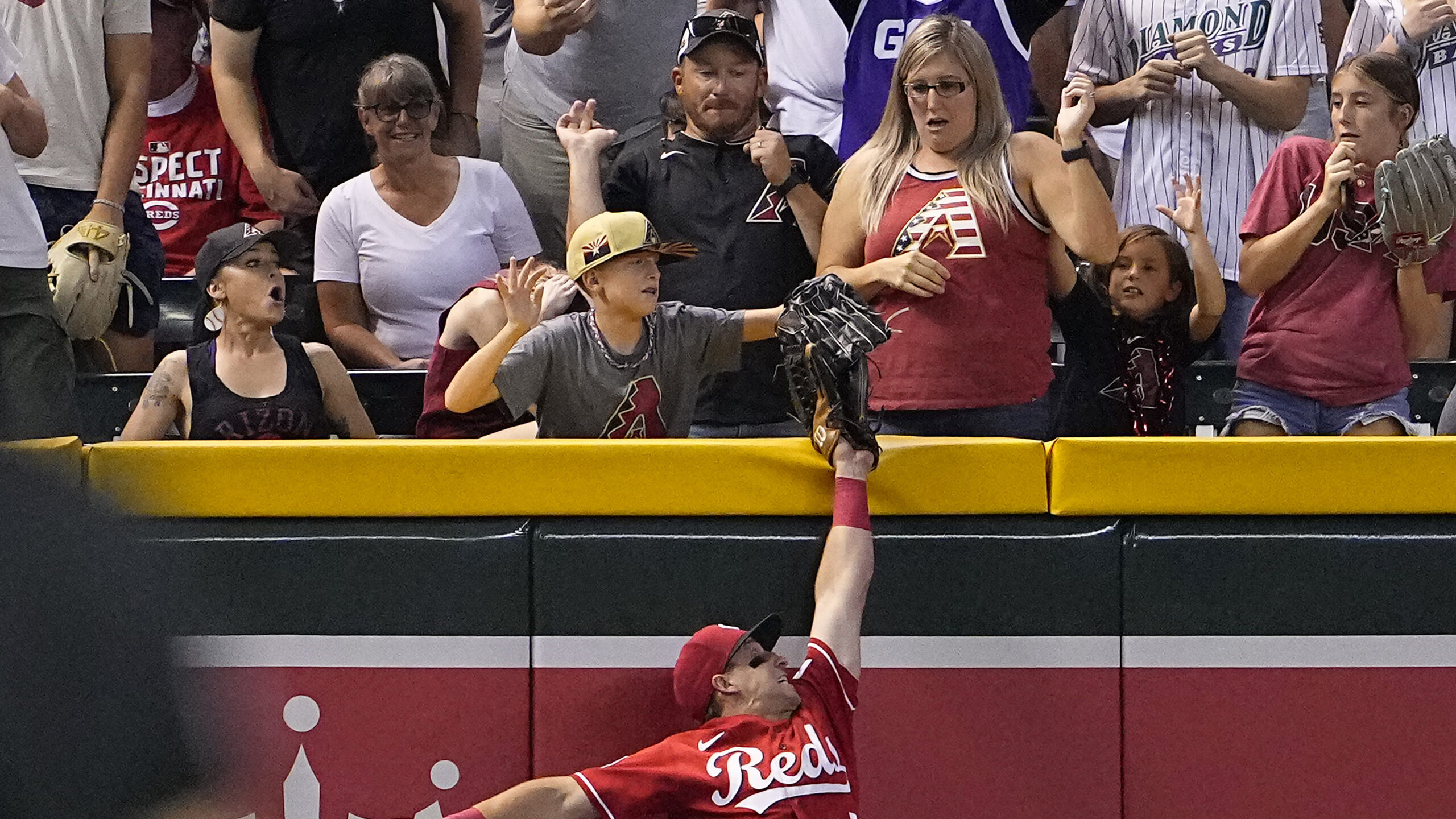 A young fan pulls the ball out of the glove of Cincinnati Reds' Spencer Steer on a ball hit by Ariz...