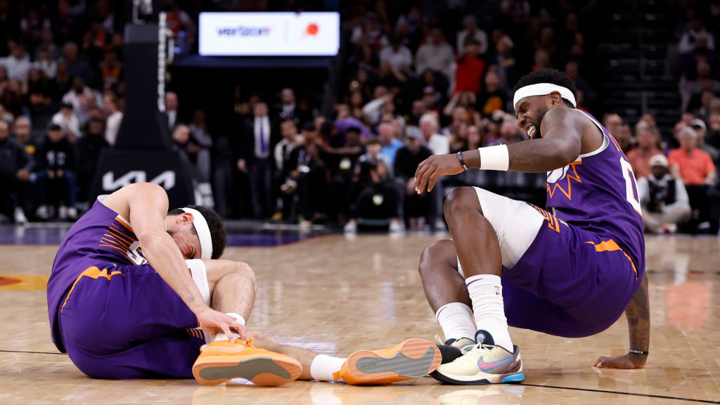 Devin Booker #1 (L) and Royce O'Neale #00 of the Phoenix Suns react after an apparent injury during...