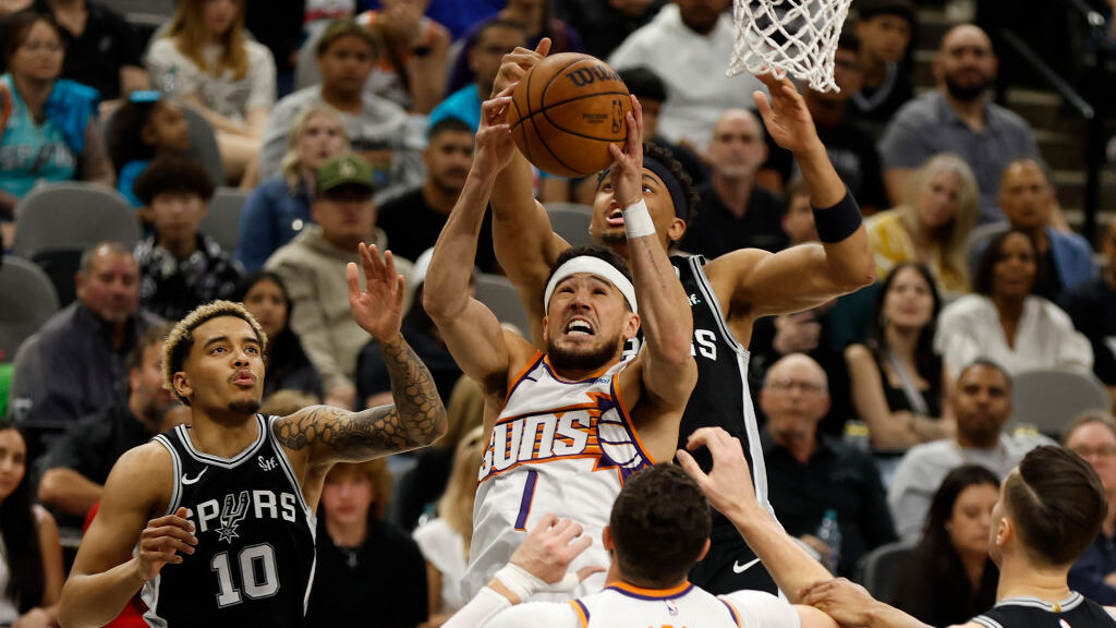 Devin Booker #1 of the Phoenix Suns drives in front of Keldon Johnson #3 of the San Antonio Spurs i...