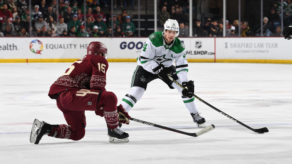 Miro Heiskanen #4 of the Dallas Stars skates with the puck while being defended by Alex Kerfoot #15...