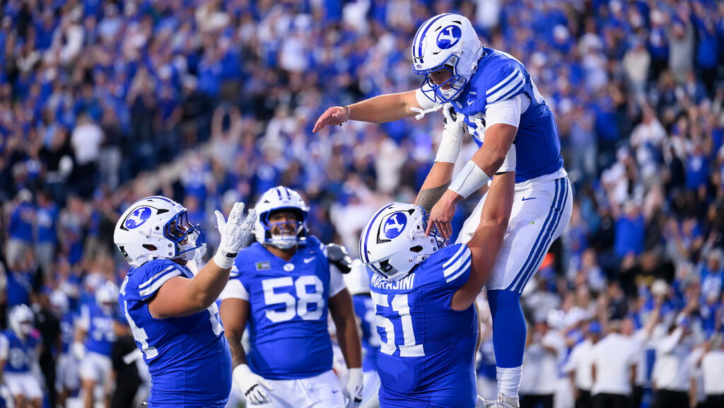 BYU offensive lineman Sonny Makasini lifts quarterback Bear Bachmeier....