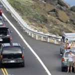 Bystanders wave as a motorcade carrying President Barack Obama drives along the road on the east coast of Oahu, Hawaii, Tuesday, Dec. 29, 2009. (AP Photo/Chris Carlson)