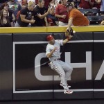 Philadelphia Phillies left fielder Raul Ibanez leaps against the wall as a fan interferes with his catch-attempt on fly ball hit by Arizona Diamondbacks' Chris Young in the sixth inning of a baseball game Saturday, April 24, 2010, in Phoenix. The hit was ruled a double. (AP Photo/Paul Connors)