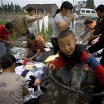 Chinese earthquake survivors make selection of donated clothes when a boy plays on a tricycle in Luoshui Town of Shifang, China's southwest Sichuan province, Saturday, June 7, 2008. (AP Photo/Alexander F. Yuan)
