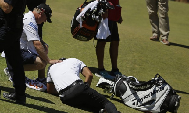 Jason Day, of Australia, lies in the fairway after falling down as his caddie Colin Swatton crouche...