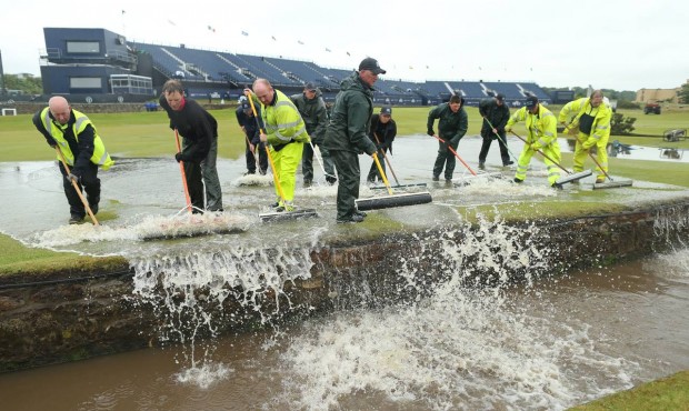Ground staff sweep flood water into the Swilcan Burn after heavy rain delayed the start of the seco...