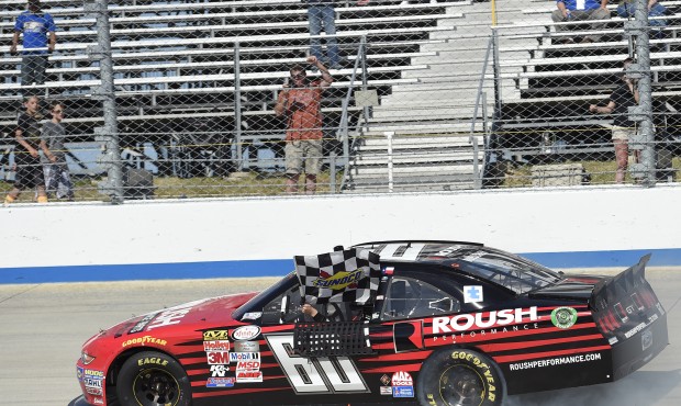Chris Buescher waves the checkered flag as he drives by the stands and celebrates after he won the ...