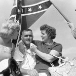 
              FILE - In this Sept. 3, 1962, file photo, Junior Johnson, center, of Ronda, N.C., poses in Victory Lane with his sister, right, and Ginger Pointevint, Miss Sun Fun U.S.A., as man dressed as a Confederate soldier holds a Confederate flag, after Johnson won the 13th Annual Southern 500 auto race at the Darlington International Raceway in Darlington, S.C. NASCAR  backed South Carolina Gov. Nikki Haley's call this week to remove the Confederate flag from the Statehouse grounds in the wake of the Charleston church massacre. Though NASCAR now bars the use of the flag in any "official capacity," they are as easy to find at NASCAR races as cutoff jeans, cowboy hats, and beer. (AP Photo/Perry Aycock, File)
            