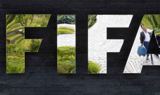 FILE – In this May 27, 2015, file photo, two persons are reflected in the FIFA logo at the FI...