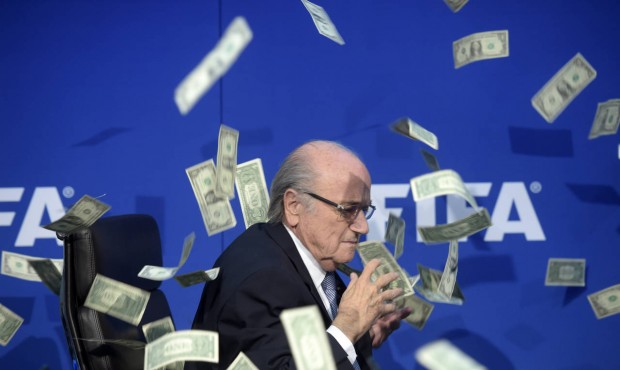 FIFA president Sepp Blatter is photographed while banknotes thrown by British comedian Simon Brodki...