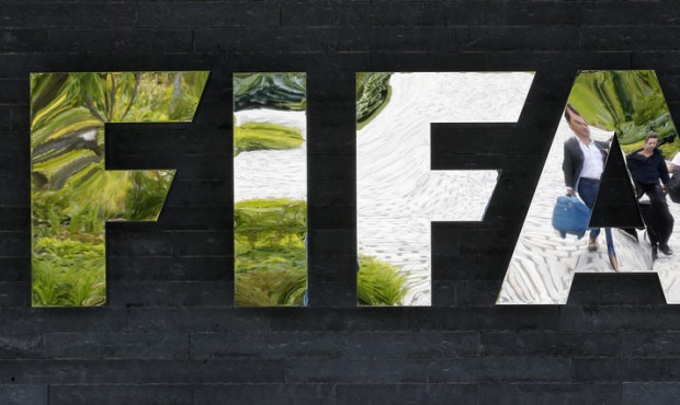 FILE – In this May 27, 2015 file photo two persons are reflected in the FIFA logo at the FIFA...