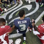 Seattle Seahawks quarterback Russell Wilson (3) holds hands with Arizona Cardinals' Calais Campbell, left, and Antonio Cromartie (31) in a prayer circle following an NFL football game, Sunday, Nov. 23, 2014, in Seattle. The Seahawks won 19-3. (AP Photo/Elaine Thompson)