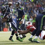 Seattle Seahawks Marshawn Lynch (24) tries to step way from a Arizona Cardinals outside linebacker Alex Okafor, lower right, as Seattle Seahawks quarterback Russell Wilson, second from left, looks on in the first half of an NFL football game, Sunday, Nov. 23, 2014, in Seattle. (AP Photo/Elaine Thompson)