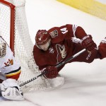 Calgary Flames' Joni Ortio, second from left, of Finland, makes a save on a shot by Arizona Coyotes' Joe Vitale (14) as Flames' Dennis Wideman (6) defends during the first period of an NHL hockey game Thursday, Jan. 15, 2015, in Glendale, Ariz. (AP Photo/Ross D. Franklin)