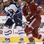 Winnipeg Jets' Dustin Byfuglien (33) passes the puck before being hit by Arizona Coyotes' Martin Hanzal (11), of the Czech Republic, during the first period of an NHL hockey game Thursday, Oct. 9, 2014, in Glendale, Ariz. (AP Photo/Ross D. Franklin)